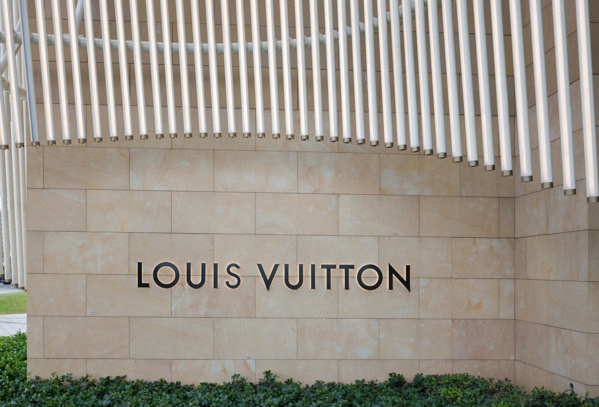 LOUIS VUITTON lettering on a sandstone wall beneath a canopy of white vertical light tubes
