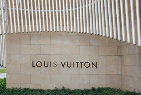 LOUIS VUITTON lettering on a sandstone wall beneath a canopy of white vertical light tubes