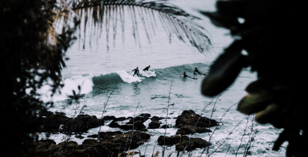 Surfers catching waves near rocky shore
