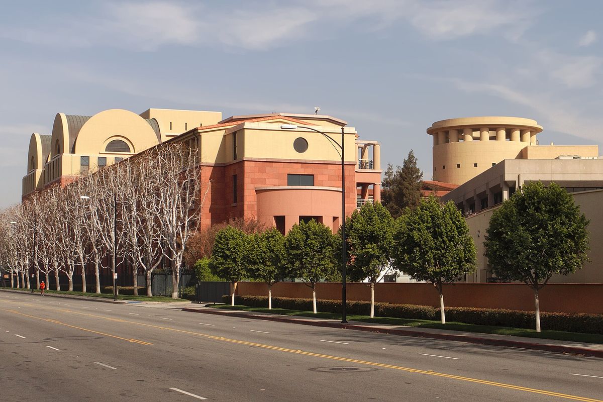 The Team Disney building in Burbank, a salmon and cream building with curved rooftop forms, seen across a wide street lined with trees
