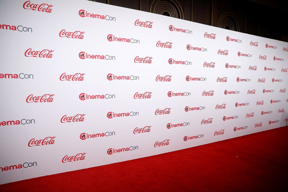 A red carpet in front of a white step-and-repeat wall printed with CinemaCon and Coca-Cola logos