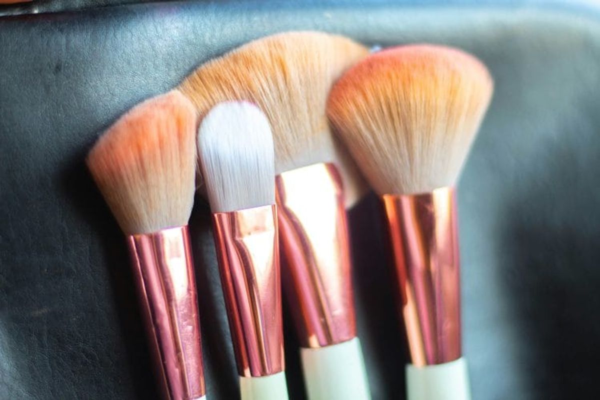 Four makeup brushes with copper ferrules on leather.