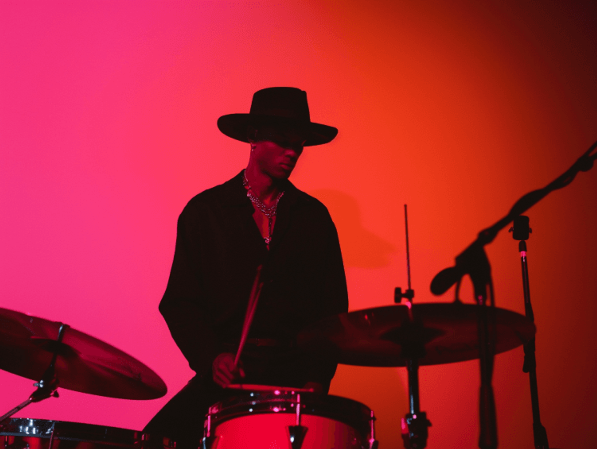 Silhouetted drummer on red-lit stage with hat.