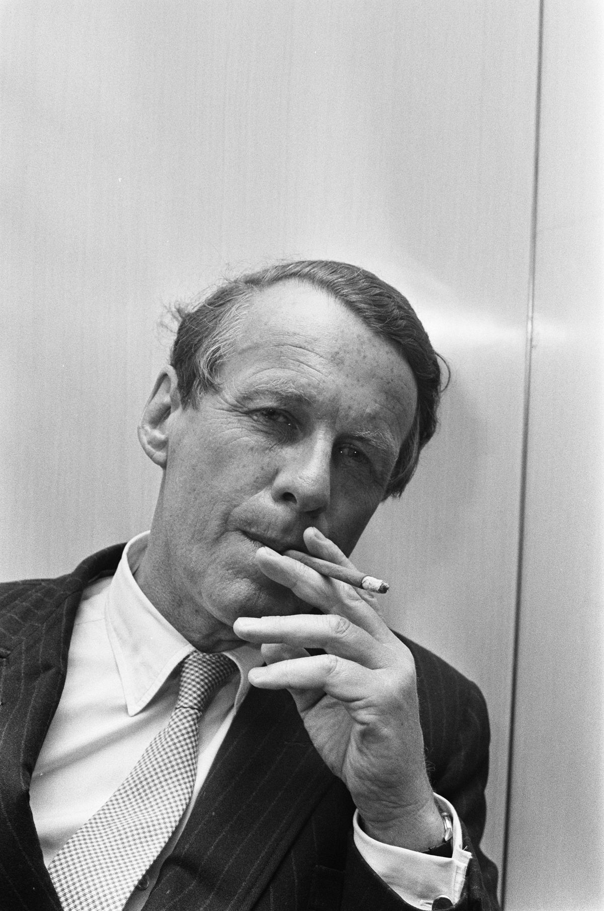 Black-and-white portrait of David Ogilvy in a pinstripe suit and tie, holding a cigarette to his lips
