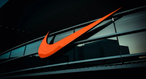 A large orange Nike swoosh sign mounted on the dark glass facade of a building at dusk