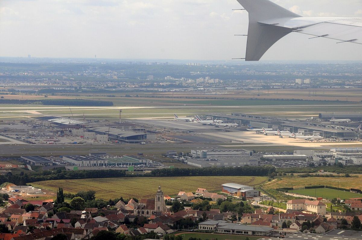 Aerial view from an airliner window of Paris-Charles de Gaulle Airport, with Air France jets at the terminals and a village in the foreground