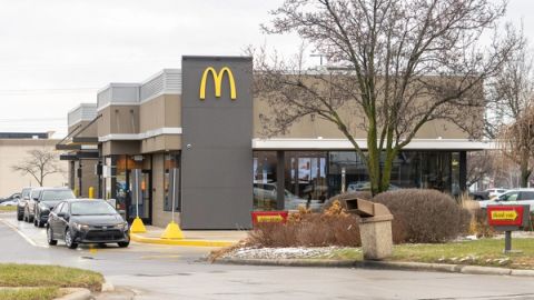 Cars lined up in the drive-thru lane of a McDonald's restaurant with a dark tower carrying the Golden Arches logo, bare trees and an overcast sky, Macomb County, Michigan