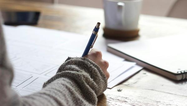 Person writing in a notebook at a clean workspace with natural light