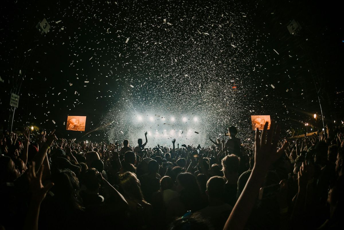 Large outdoor festival crowd with colorful stage lighting at dusk