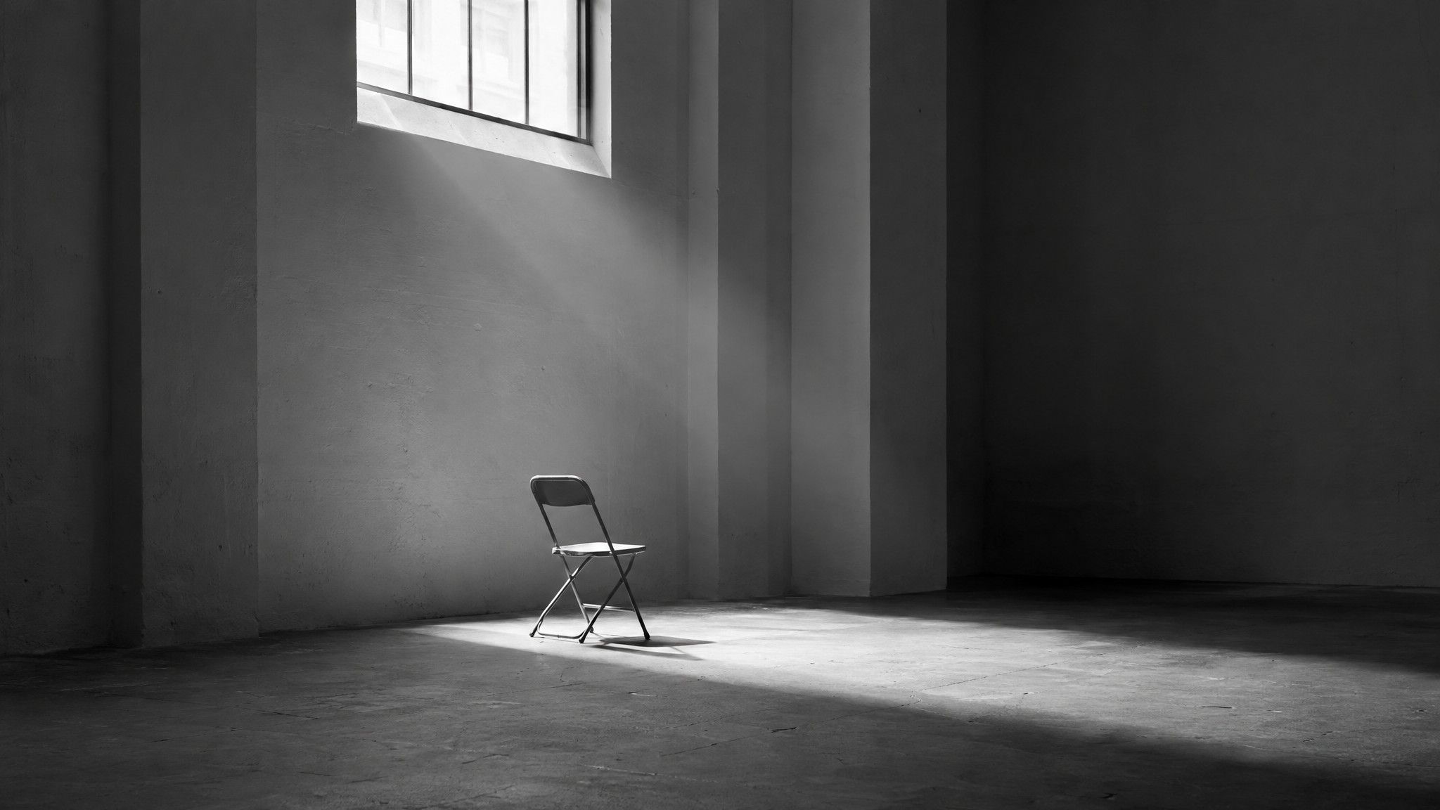 Single folding chair in a shaft of light in a concrete hall