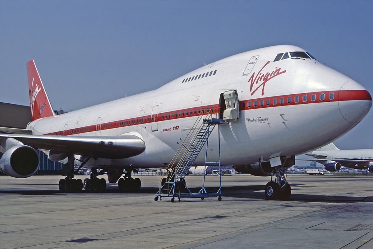 Virgin Atlantic Boeing 747 in white and red livery with Maiden Voyager written on the nose, parked with boarding stairs at the front door