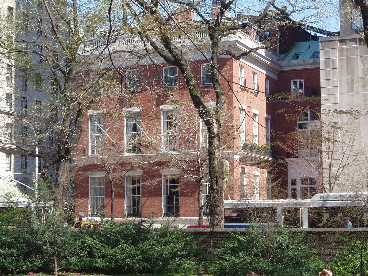 The red brick Knickerbocker Club building with white window trim, seen through bare trees from Central Park