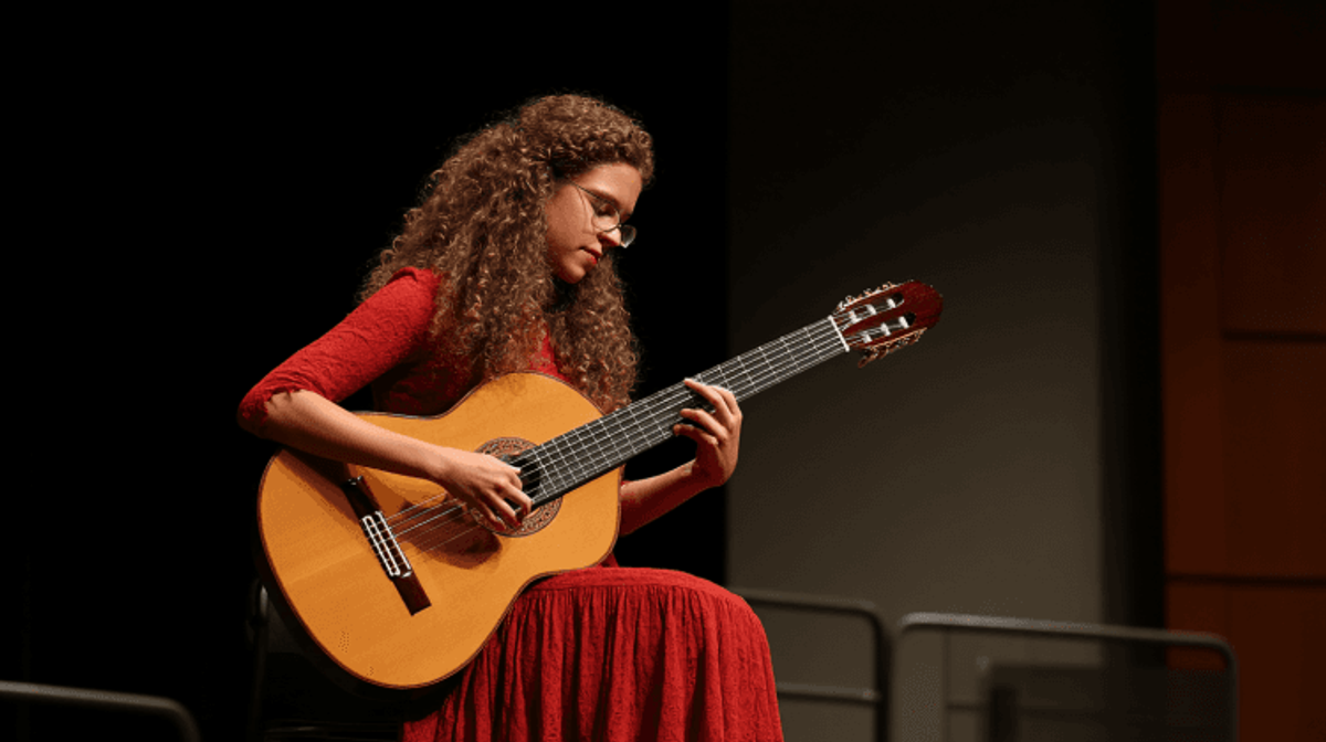 Woman playing classical guitar on stage.