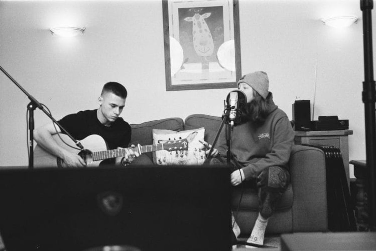 Two musicians recording in a living room setting.