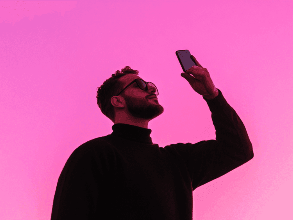 Silhouette of person with phone against pink sky.