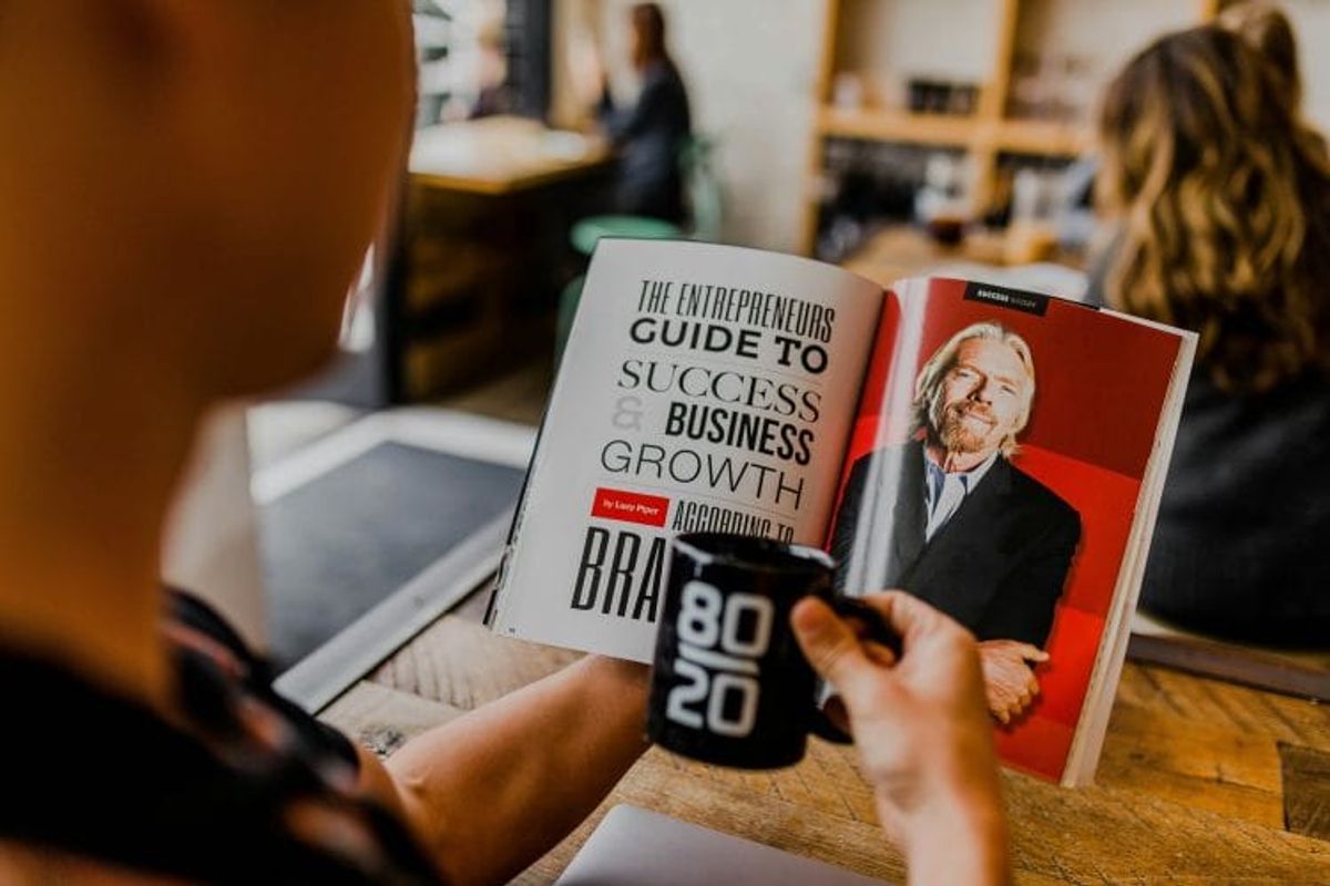 Person reading business growth magazine with coffee mug.