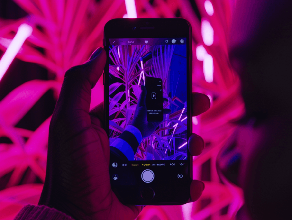 Hand holding phone with neon pink lights.