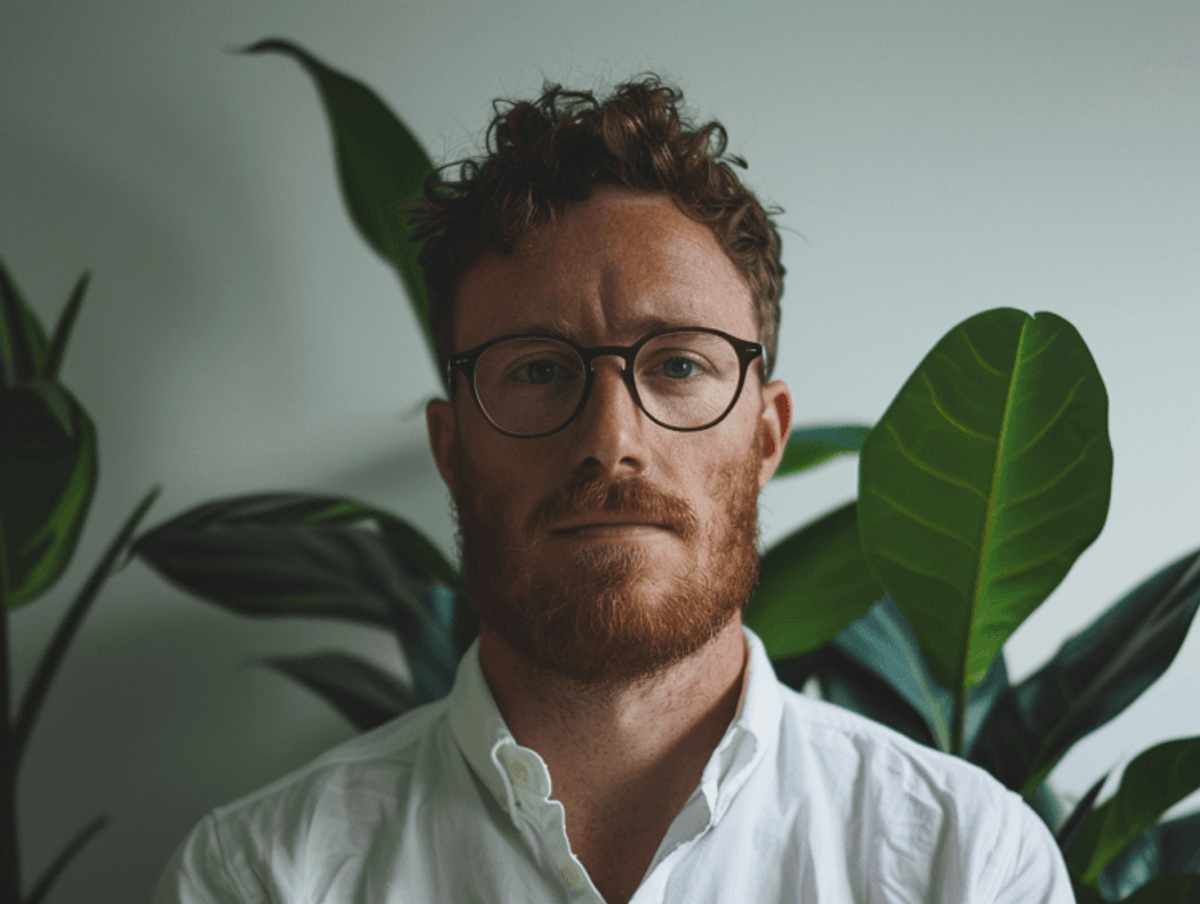Person with glasses and beard, plants in background.