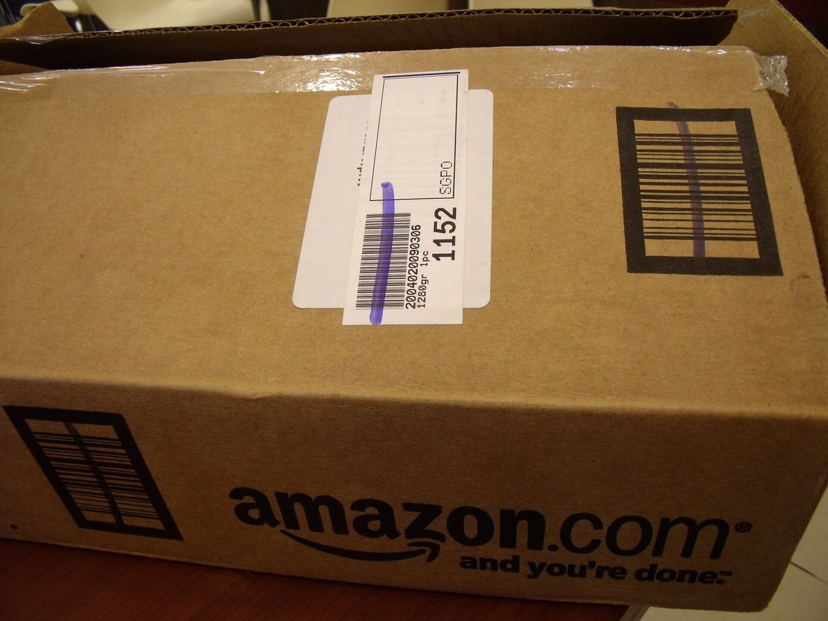 Close-up of a brown cardboard shipping box printed with the amazon.com logo and the slogan and you're done, with a barcode label on top
