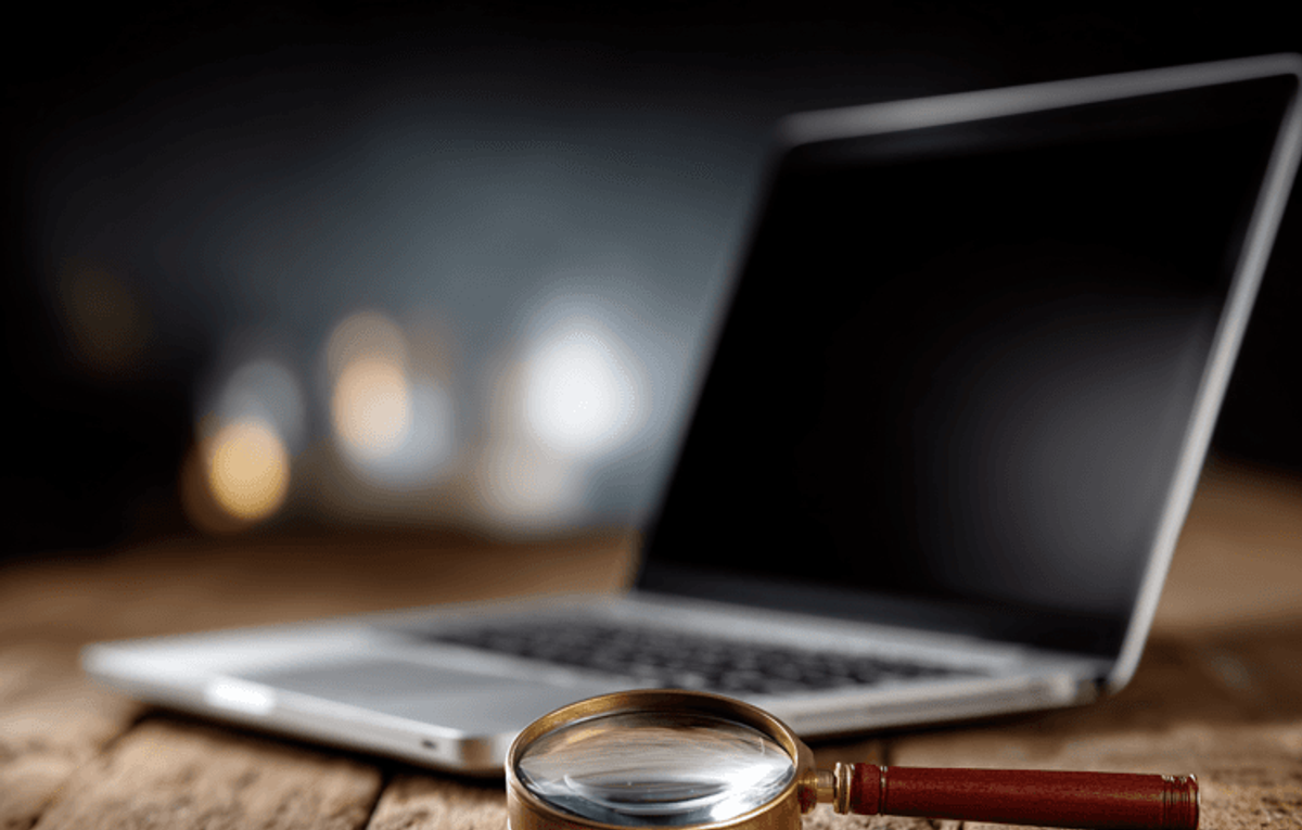 Laptop with magnifying glass on wooden table