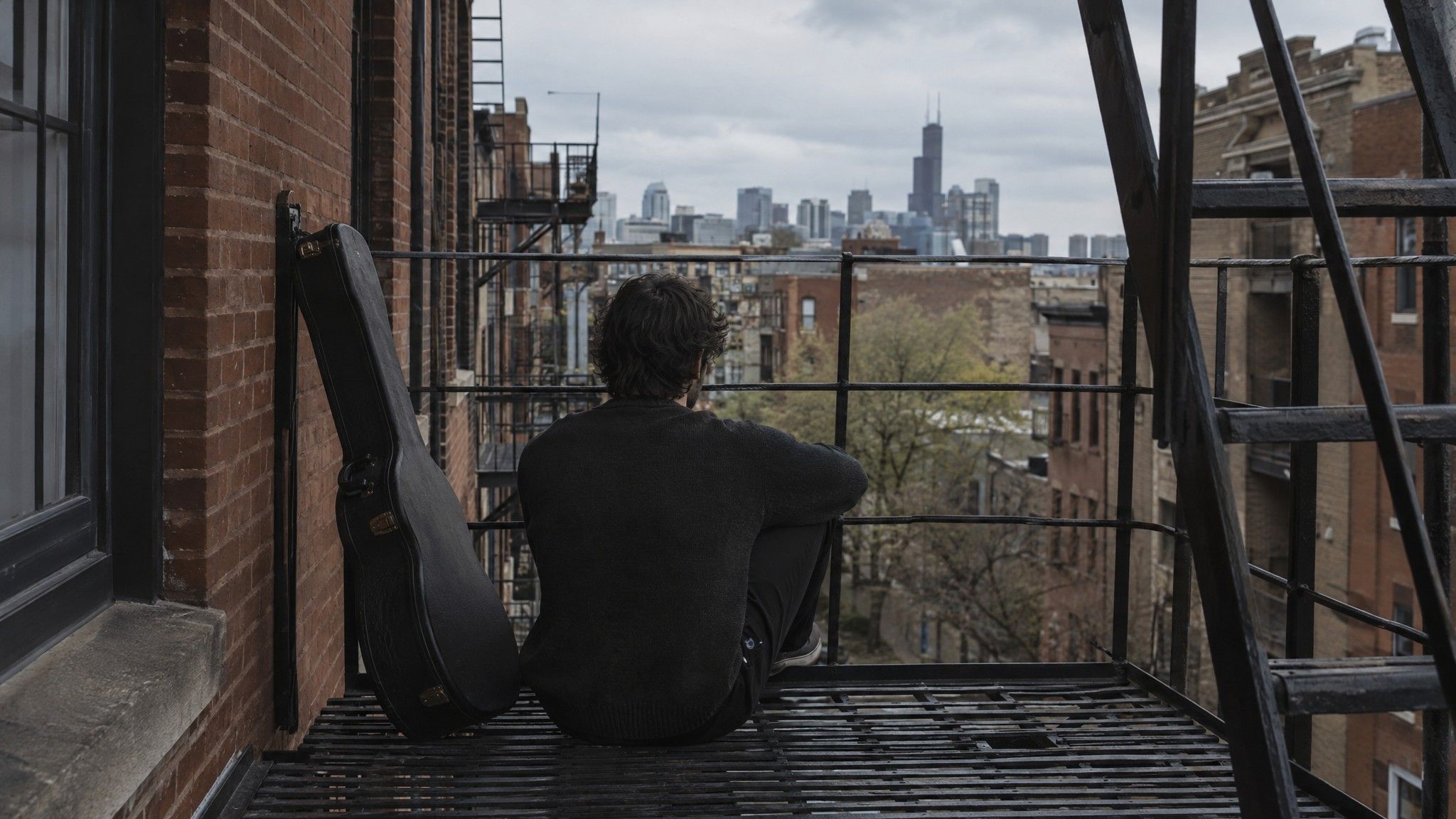 Musician seen from behind on a city fire escape with a guitar case