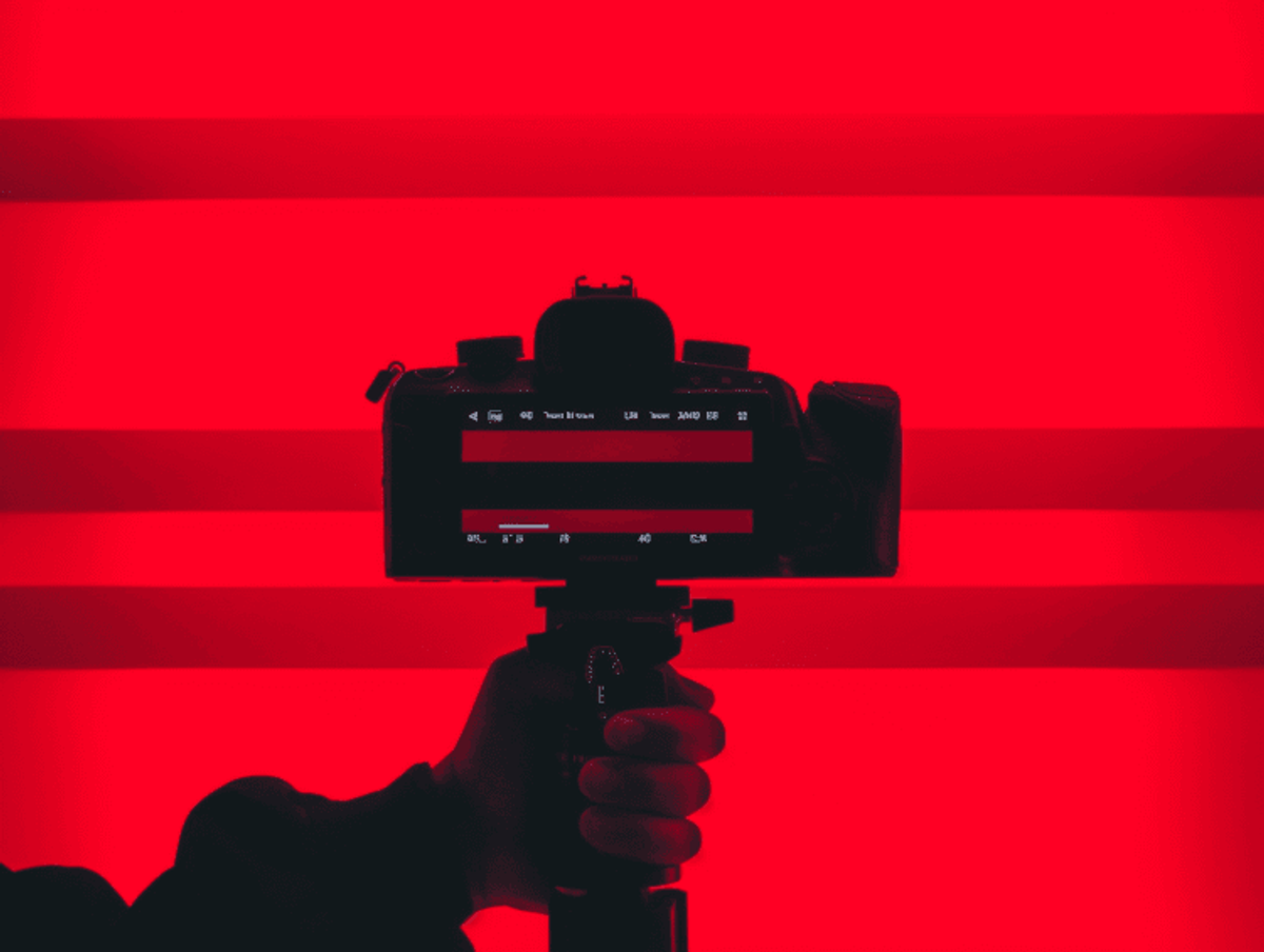 Silhouette of camera against vibrant red background.