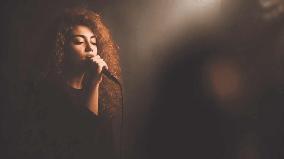 Woman singing into a microphone under spotlight