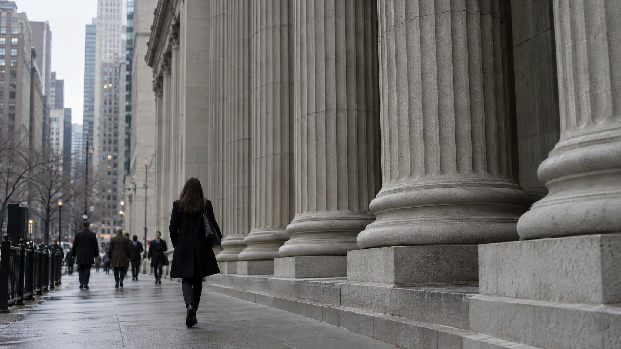 Woman in a dark coat walking past stone columns in a financial district