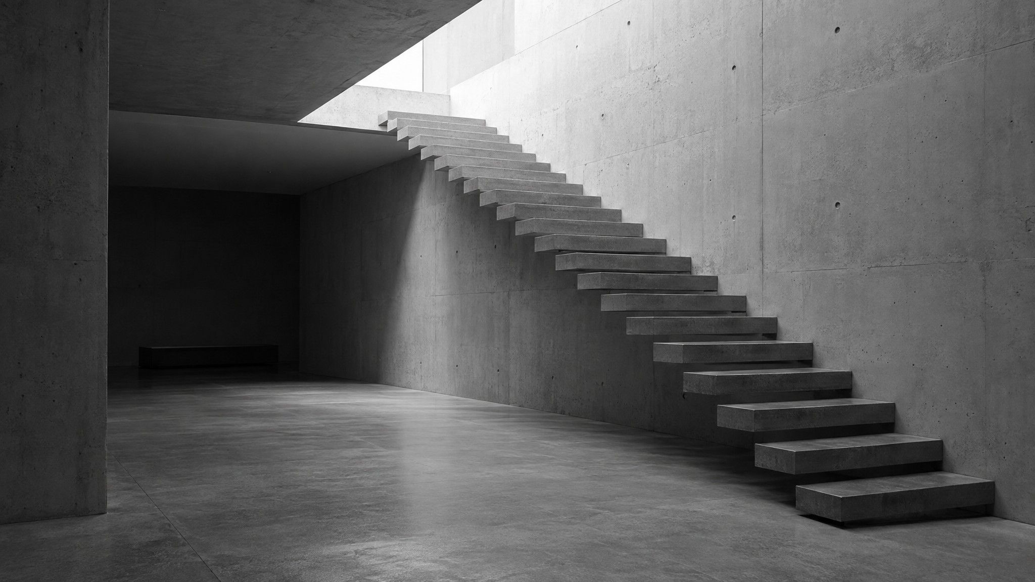 Concrete staircase rising toward a skylight in deep shadow