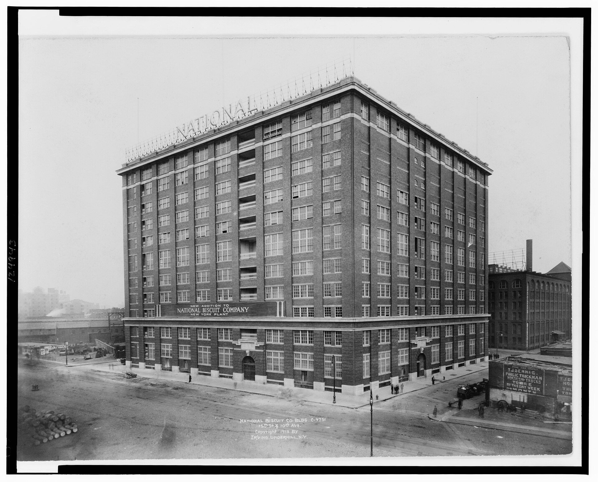 Black-and-white 1913 photograph of a tall brick factory building on a street corner, with National Biscuit Company signs on the roof and above the ground floor