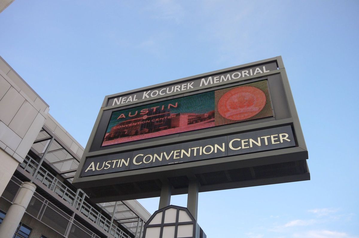 The tall sign of the Neal Kocurek Memorial Austin Convention Center against a blue sky, with an LED screen showing the Austin Convention Center logo