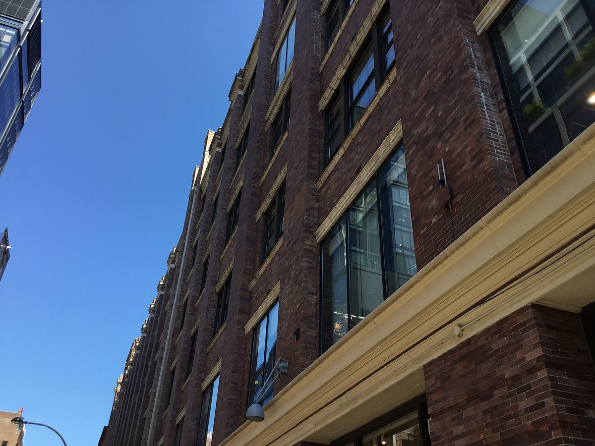 Upward view of a tall red-brick former factory building with large industrial windows against a clear blue sky
