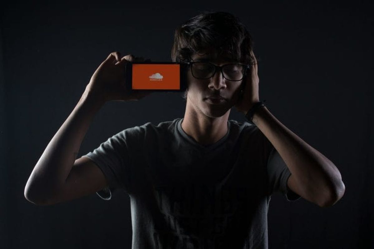 Person with smartphone displaying SoundCloud logo in darkness.
