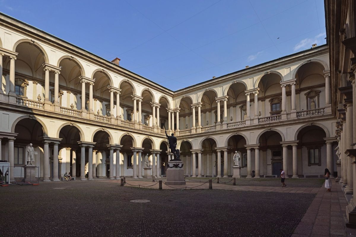The arcaded courtyard of Palazzo Brera in Milan, with two levels of paired columns, marble statues under the arches and a bronze statue on a pedestal in the middle