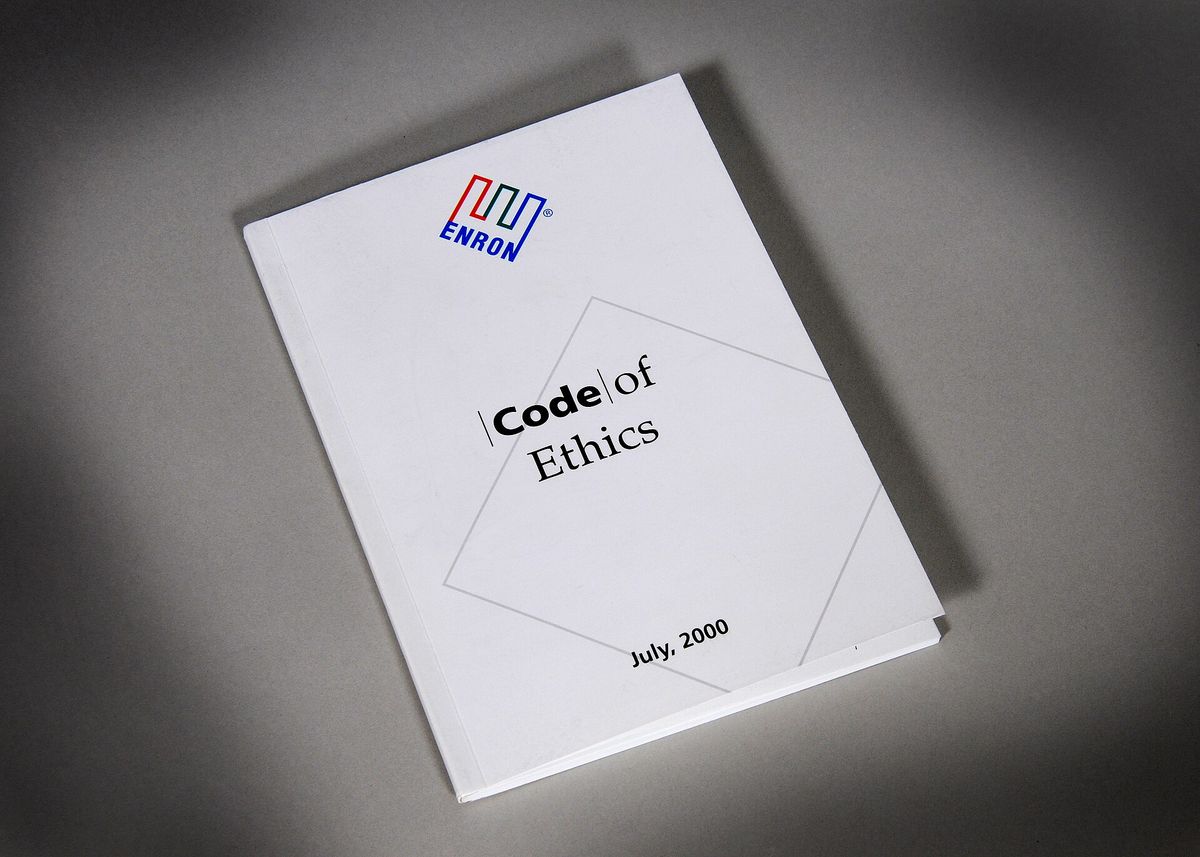 A white booklet with the Enron logo and the title "Code of Ethics," dated July 2000, lying at an angle on a grey surface