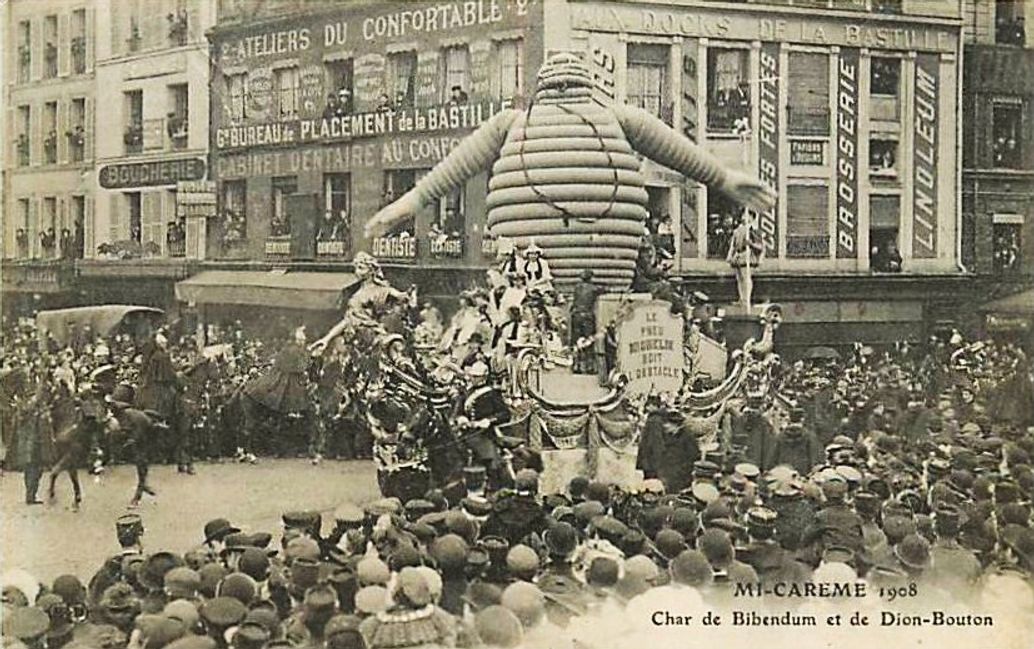 A 1908 postcard of a giant inflatable Bibendum on a De Dion-Bouton parade float in a crowded Paris street during Mi-Carême
