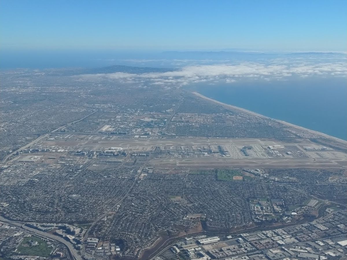 Aerial view of Los Angeles International Airport and its runways beside the Pacific coast, with surrounding neighborhoods in the foreground