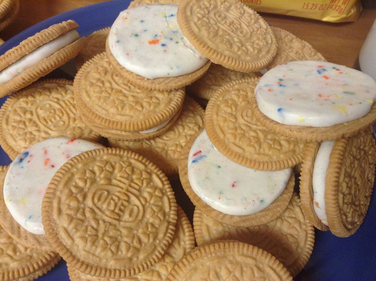 A pile of golden Oreo-style sandwich cookies with white creme dotted with colored sprinkles, some pulled apart to show the filling