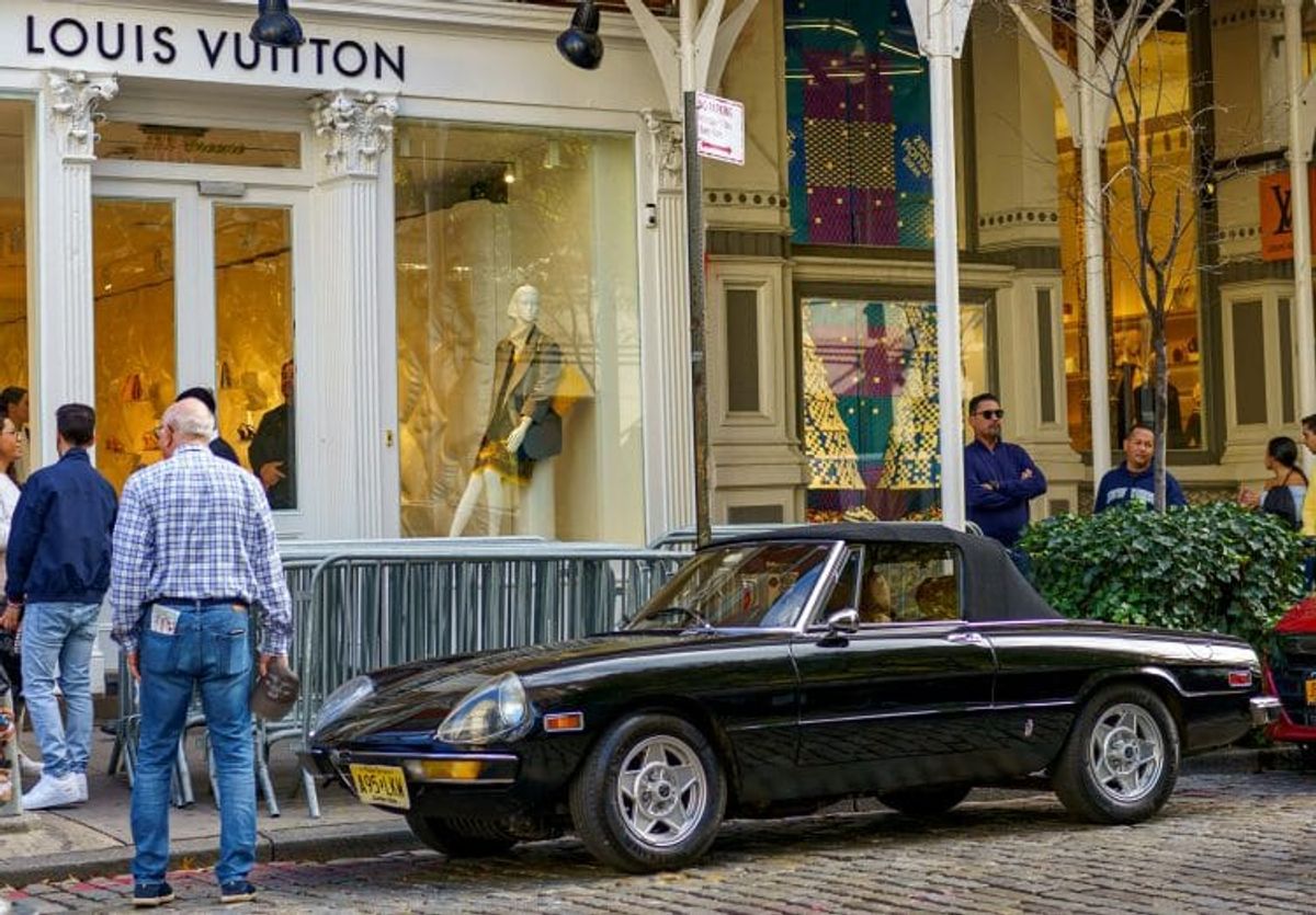 Black car outside Louis Vuitton store entrance.