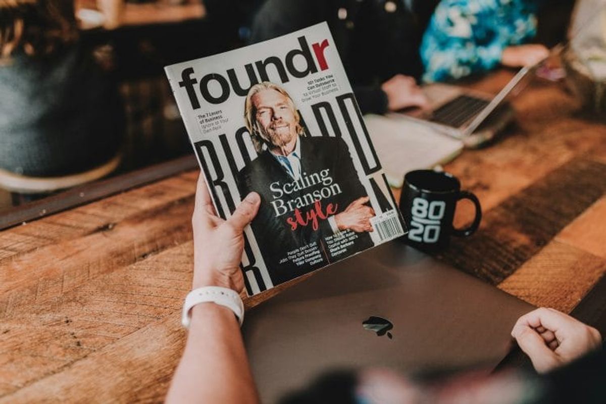 Person holding Foundr magazine at wooden table.