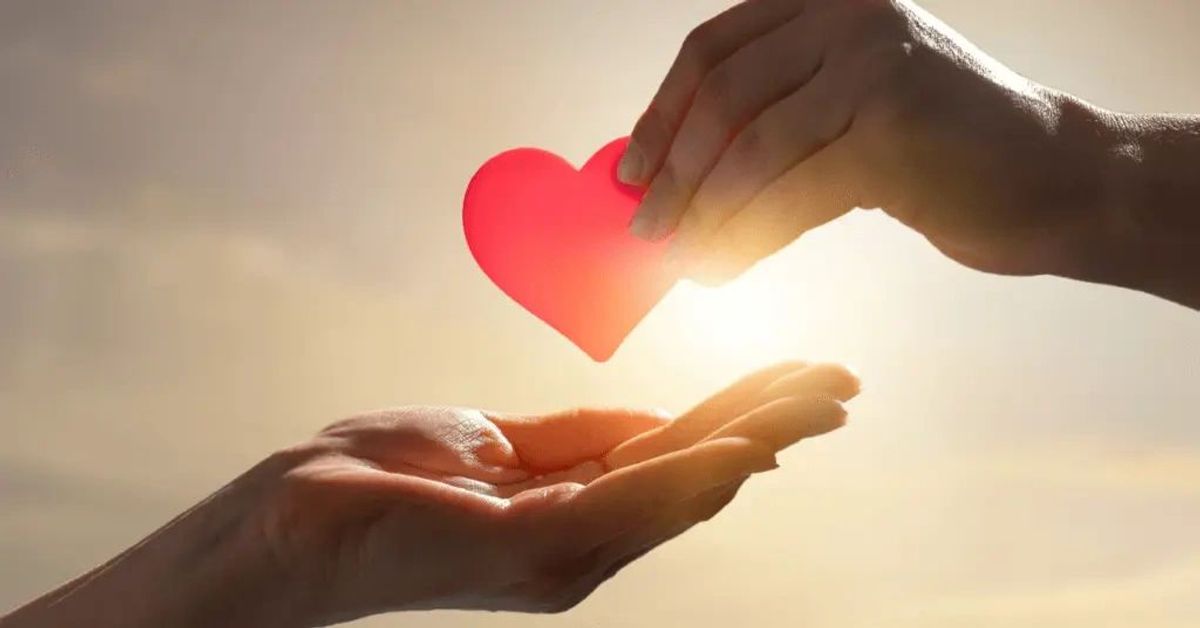 Hand passing a heart to another at sunset