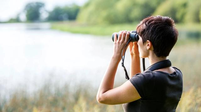 Woman looking through binoculars at a lake