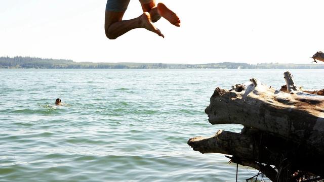 Two people jumping off of a log into the lake