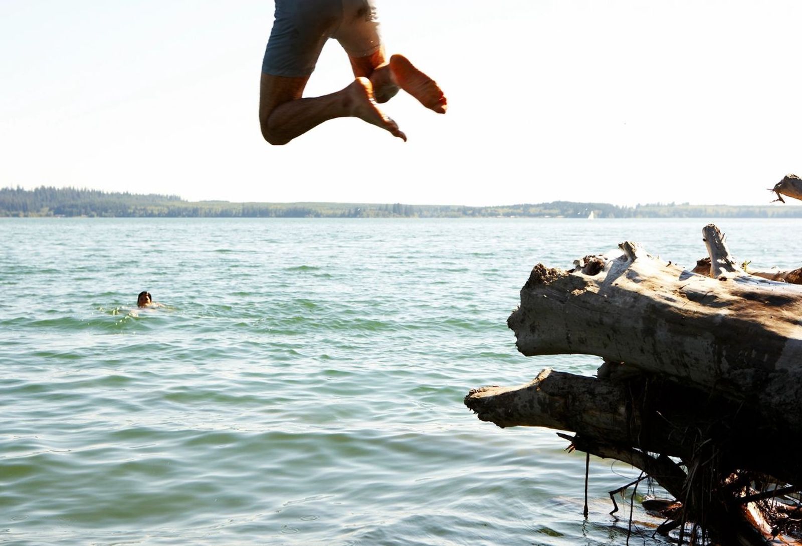 Two people jumping off of a log into the lake