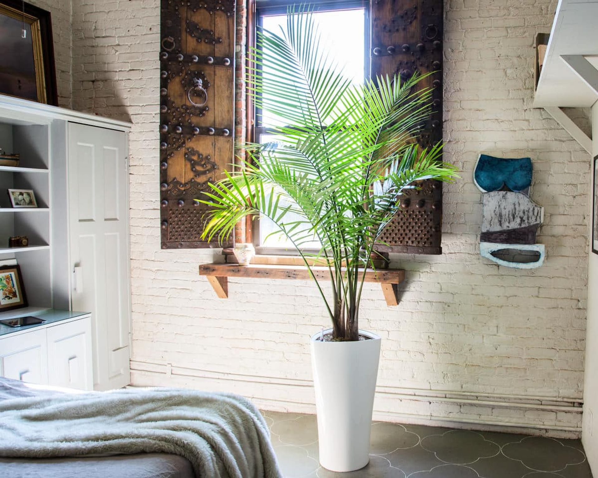 Cozy modern living room with indoor plant in white pot, decorative metal wall art, and soft grey throw on sofa beside white brick wall