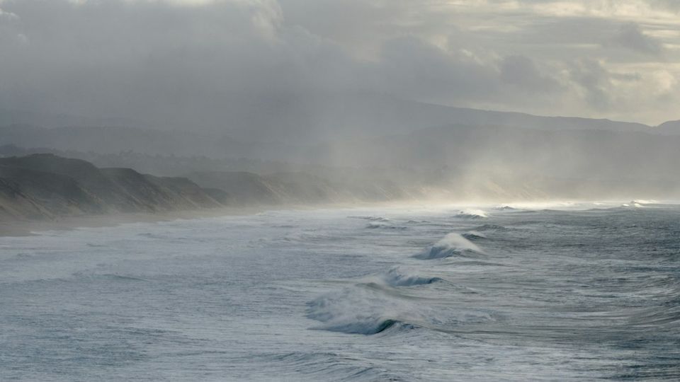 Waves crash on a misty coastline under a cloudy sky