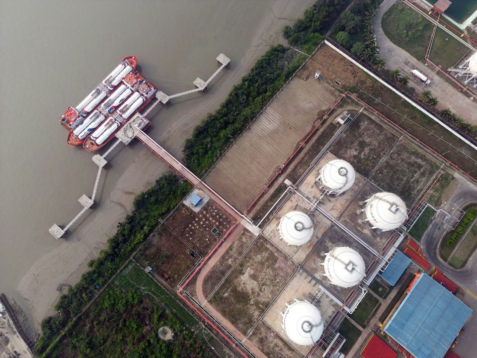Aerial view of a tanker ship docked at a terminal with white storage tanks