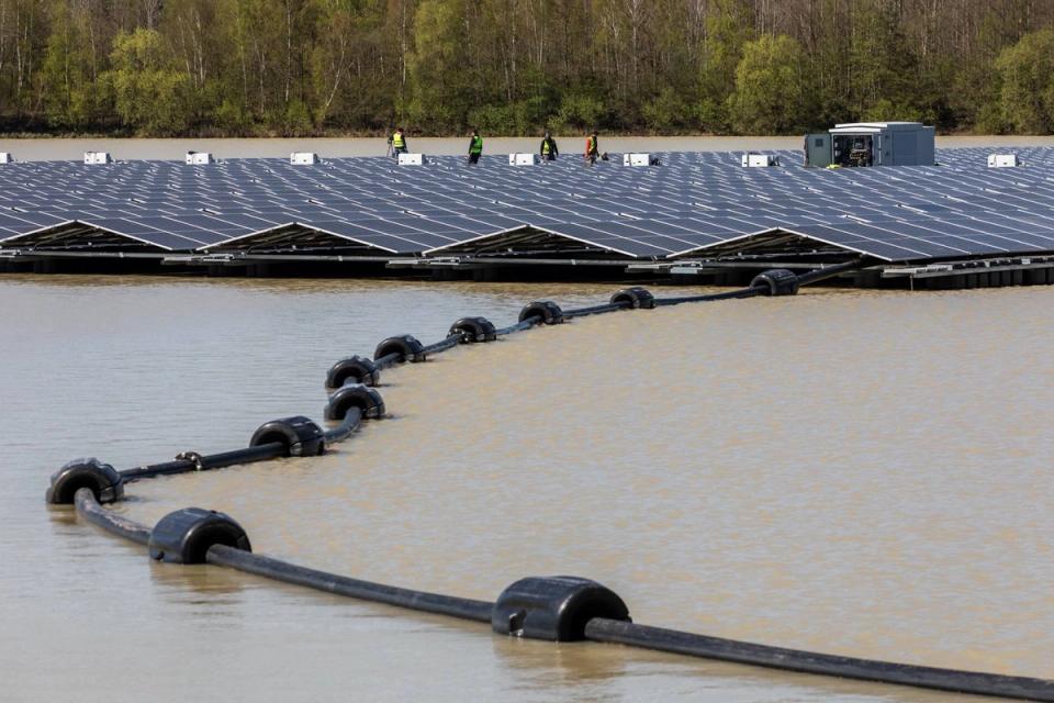 A floating solar array on a lake, with a black floating boom curving across the water in the foreground.