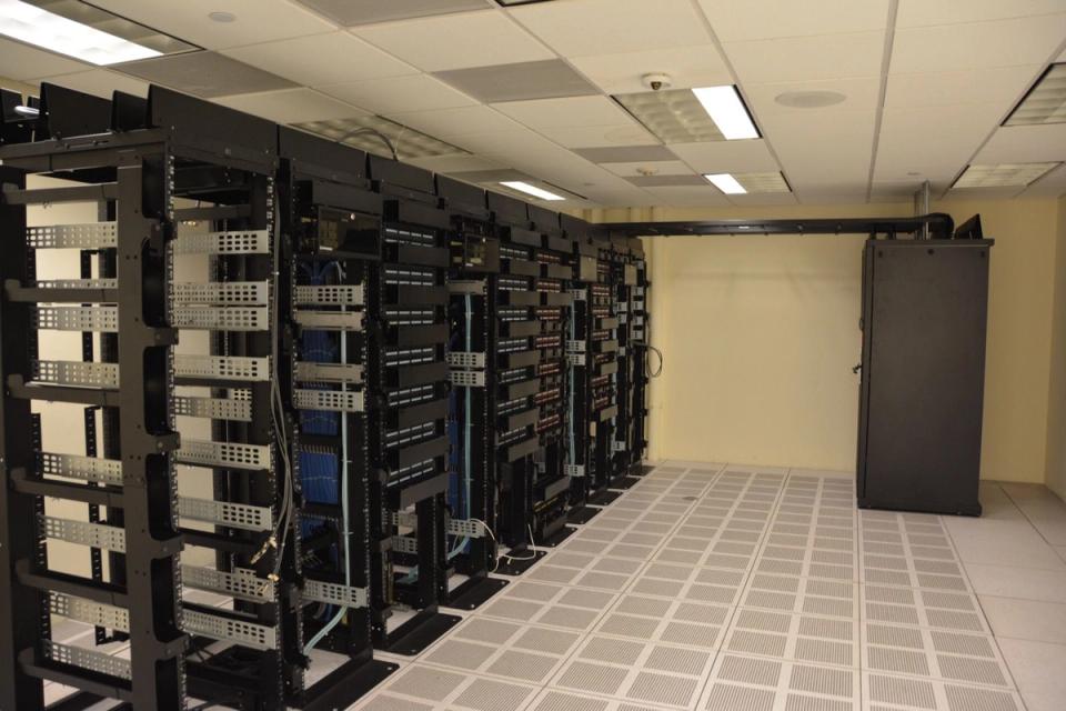 Rows of black server racks and network cabling inside a data centre room.