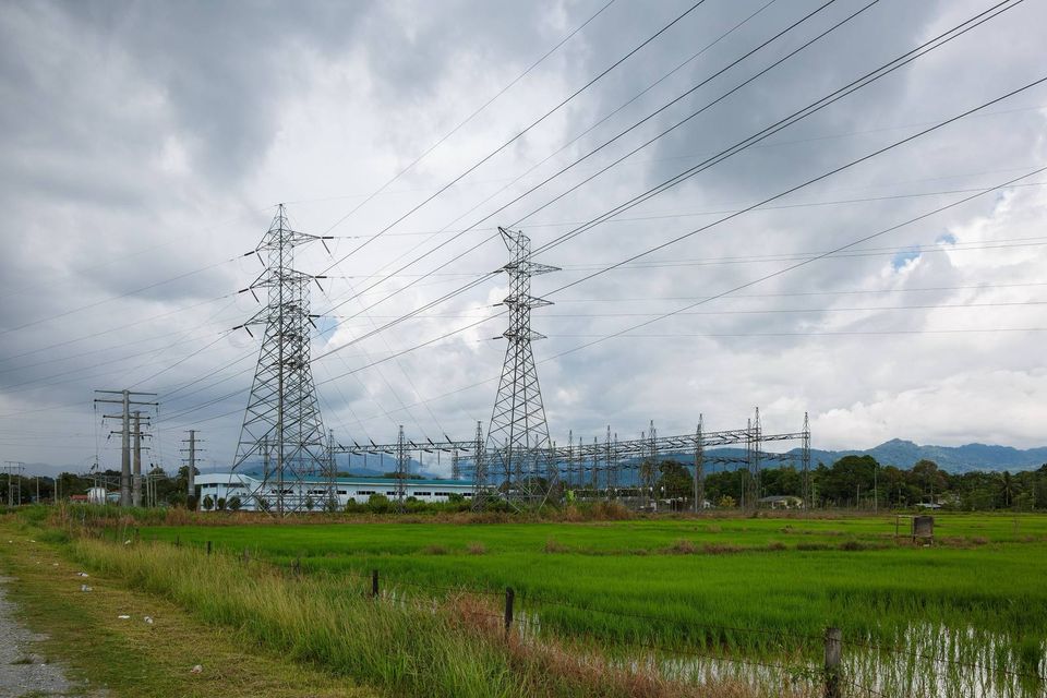High-voltage transmission pylons and a substation beside green rice paddies under heavy clouds in Papar, Sabah, Malaysia.